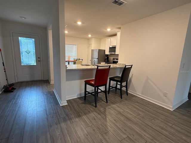 kitchen featuring visible vents, a breakfast bar, stainless steel appliances, white cabinetry, and dark wood-style flooring