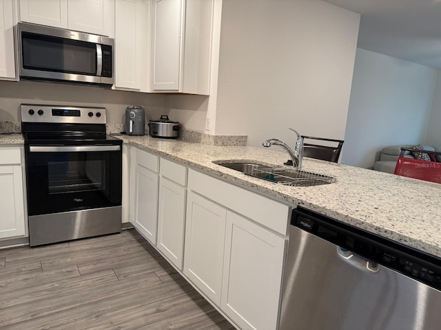 kitchen featuring light wood-type flooring, a sink, light stone counters, white cabinetry, and appliances with stainless steel finishes