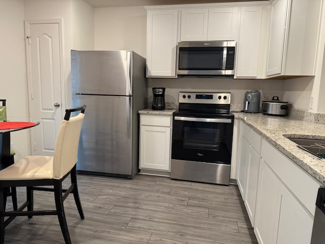 kitchen with light wood-style flooring, white cabinets, stainless steel appliances, and light stone countertops