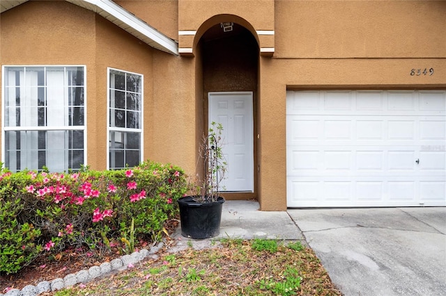 entrance to property with stucco siding, driveway, and a garage