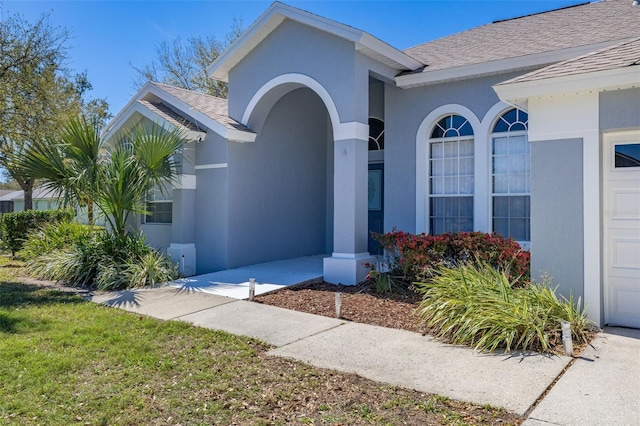 property entrance with stucco siding and a shingled roof