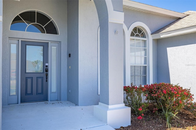 entrance to property featuring stucco siding and roof with shingles