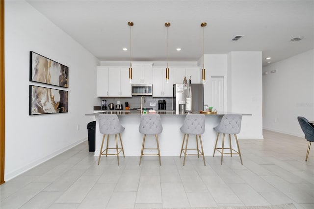 kitchen with a breakfast bar area, visible vents, a large island with sink, stainless steel appliances, and tasteful backsplash