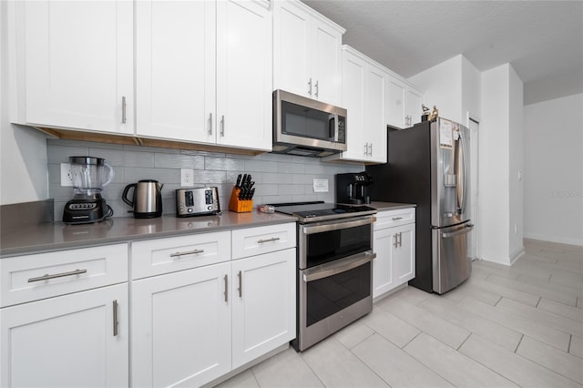 kitchen featuring backsplash, baseboards, appliances with stainless steel finishes, white cabinets, and a textured ceiling