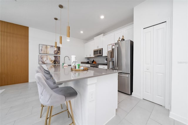 kitchen featuring a kitchen island with sink, white cabinetry, appliances with stainless steel finishes, a breakfast bar area, and decorative backsplash