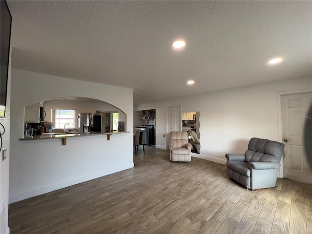 living room featuring baseboards, recessed lighting, wood finished floors, arched walkways, and a textured ceiling