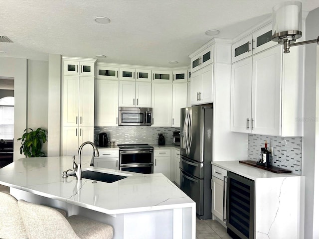 kitchen with a sink, decorative backsplash, appliances with stainless steel finishes, and beverage cooler