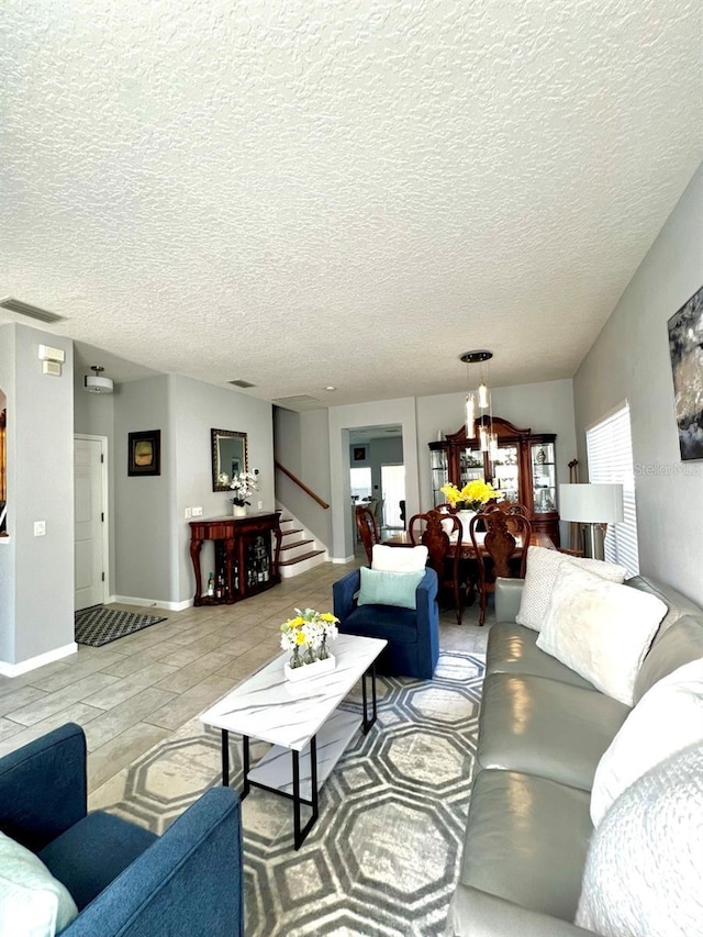 living area featuring stairway, visible vents, a textured ceiling, and baseboards