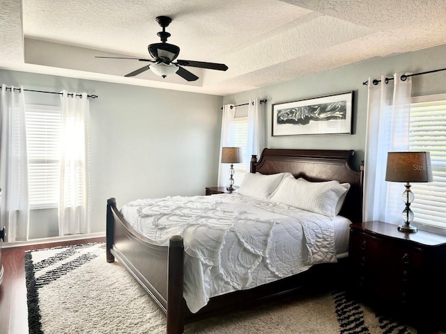 bedroom with a raised ceiling, multiple windows, and a textured ceiling