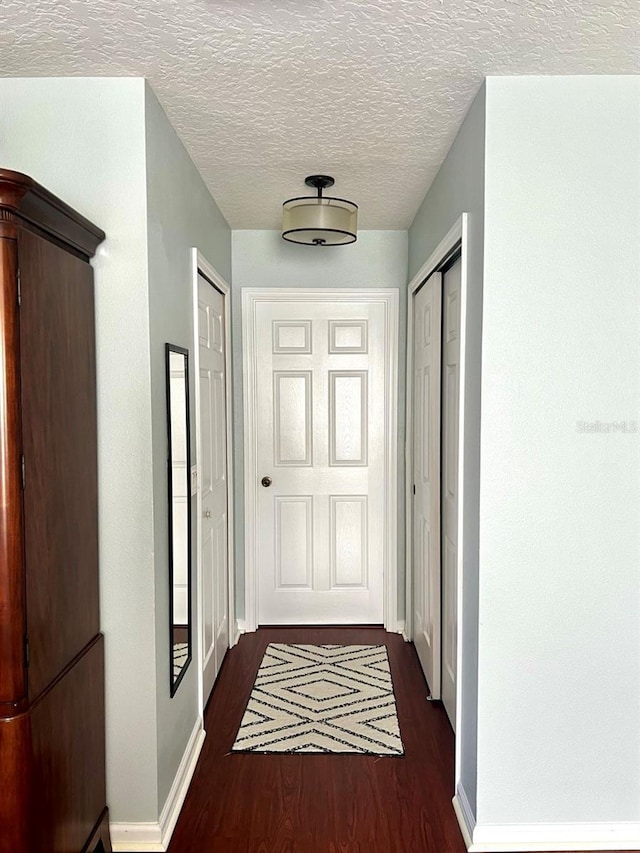 hallway with baseboards, dark wood-type flooring, and a textured ceiling