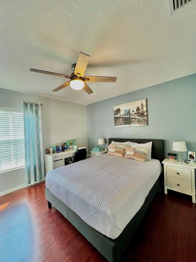 bedroom with visible vents, a textured ceiling, wood finished floors, and a ceiling fan