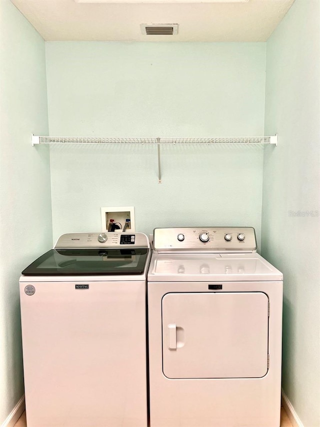 washroom featuring laundry area, washing machine and dryer, visible vents, and baseboards