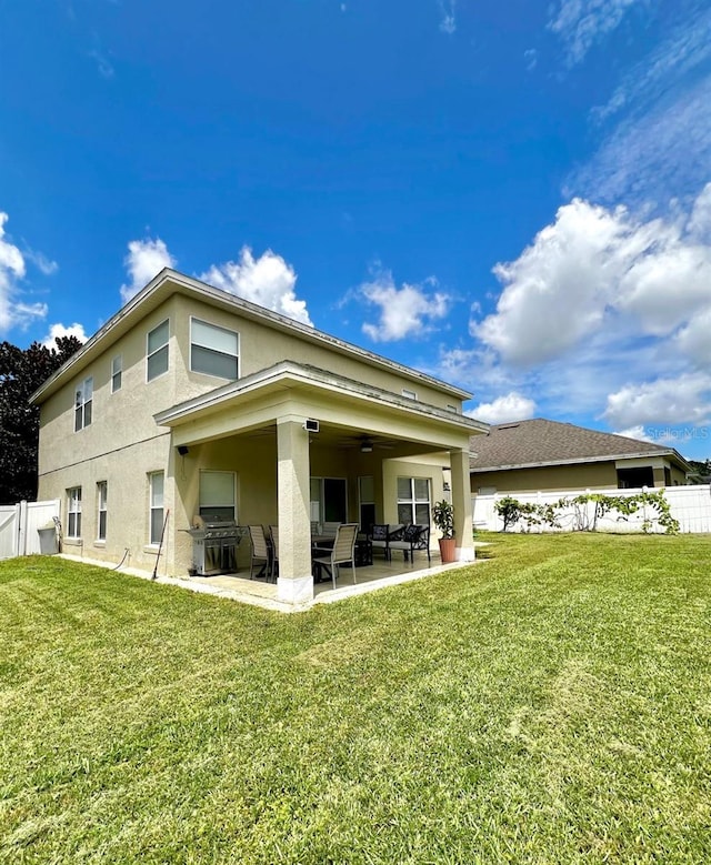 rear view of property featuring a patio area, a yard, stucco siding, and fence