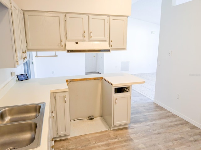 kitchen with visible vents, under cabinet range hood, light countertops, light wood-style flooring, and a sink