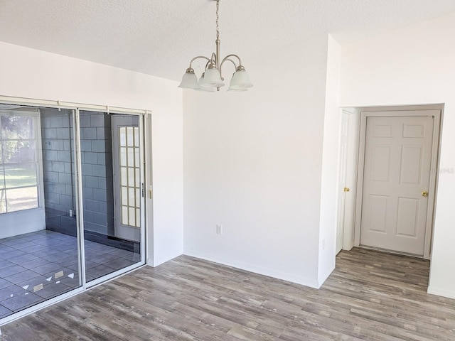 empty room featuring baseboards, a textured ceiling, an inviting chandelier, and wood finished floors