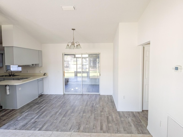 kitchen with wood finished floors, gray cabinetry, light countertops, vaulted ceiling, and a chandelier