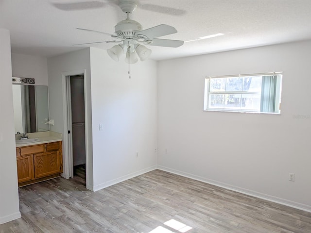 unfurnished bedroom with baseboards, ceiling fan, a sink, ensuite bathroom, and light wood-type flooring