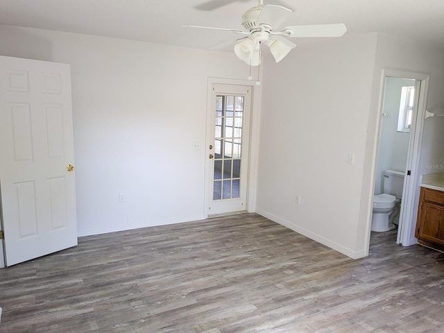 unfurnished bedroom with a ceiling fan, ensuite bathroom, baseboards, and wood finished floors