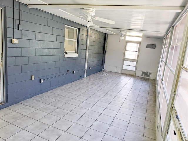 interior space with concrete block wall, a ceiling fan, and visible vents