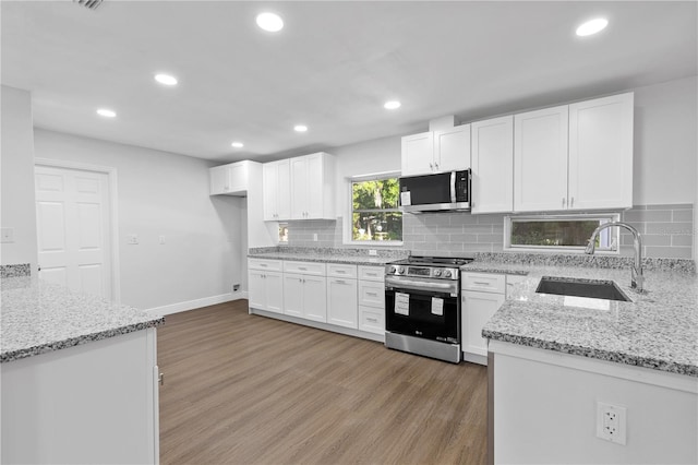 kitchen with light stone countertops, light wood-style flooring, a sink, stainless steel appliances, and white cabinets