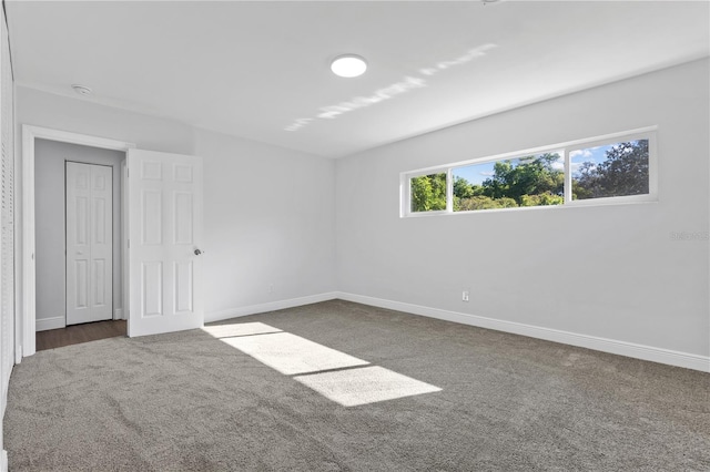 unfurnished room with baseboards and dark colored carpet