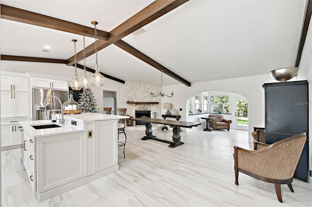 kitchen with lofted ceiling with beams, a fireplace, arched walkways, stainless steel refrigerator with ice dispenser, and open floor plan