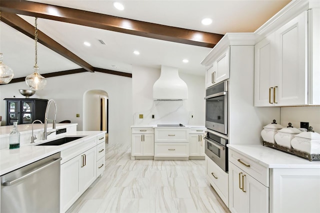 kitchen featuring custom range hood, a sink, lofted ceiling with beams, arched walkways, and appliances with stainless steel finishes