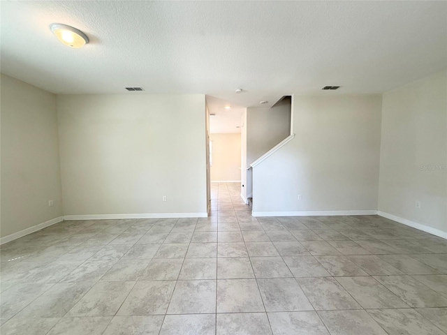 spare room featuring visible vents, baseboards, a textured ceiling, and light tile patterned flooring