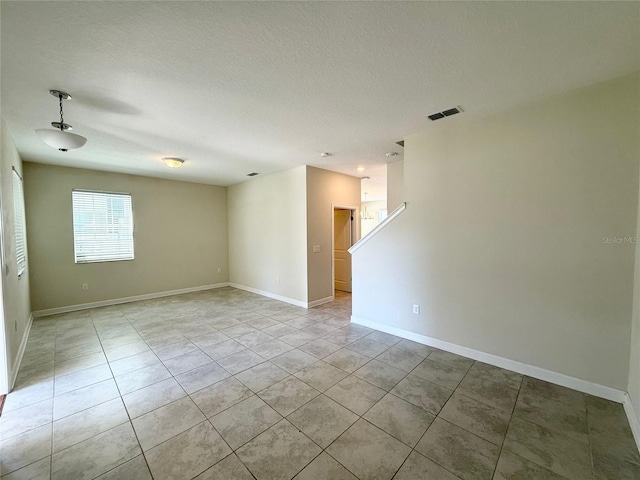 spare room featuring light tile patterned floors, baseboards, visible vents, and a textured ceiling