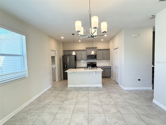 kitchen featuring a center island with sink, a sink, gray cabinetry, light countertops, and stainless steel appliances