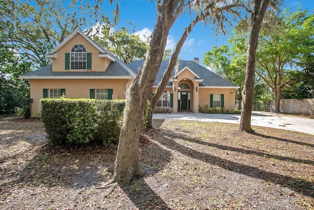 view of front facade featuring stucco siding, a shingled roof, and fence