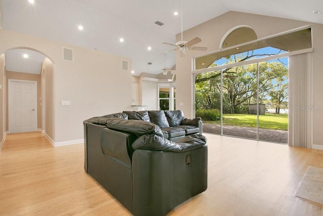 living room with arched walkways, a ceiling fan, and light wood-style floors