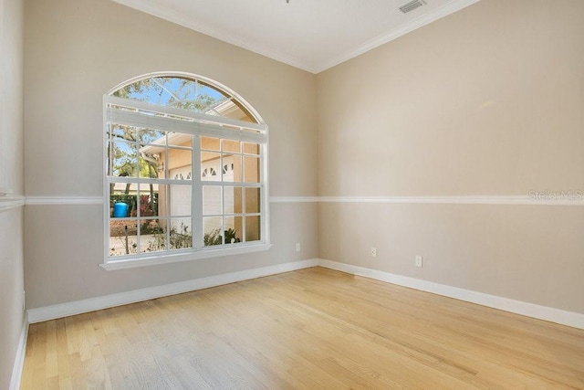 empty room with visible vents, ornamental molding, baseboards, and wood finished floors