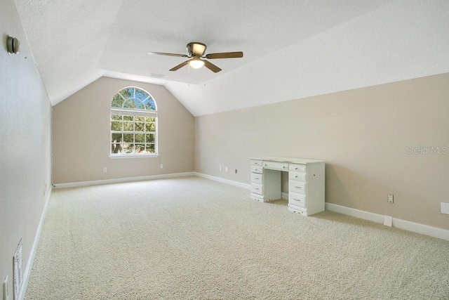 additional living space with ceiling fan, vaulted ceiling, light colored carpet, and a textured ceiling