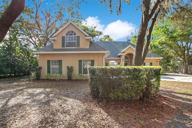 view of front of house with a shingled roof, fence, and stucco siding