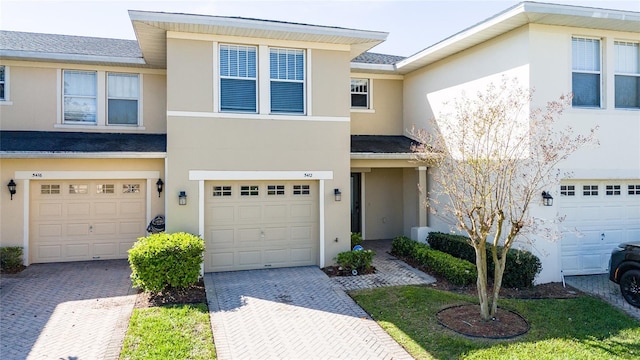 multi unit property with a shingled roof, decorative driveway, a garage, and stucco siding