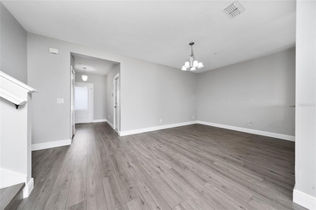 spare room featuring visible vents, baseboards, an inviting chandelier, and wood finished floors