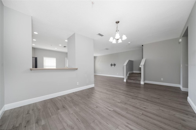 unfurnished living room with a chandelier, visible vents, stairs, and wood finished floors