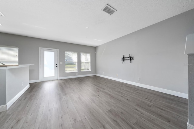 unfurnished living room featuring a textured ceiling, wood finished floors, visible vents, and baseboards