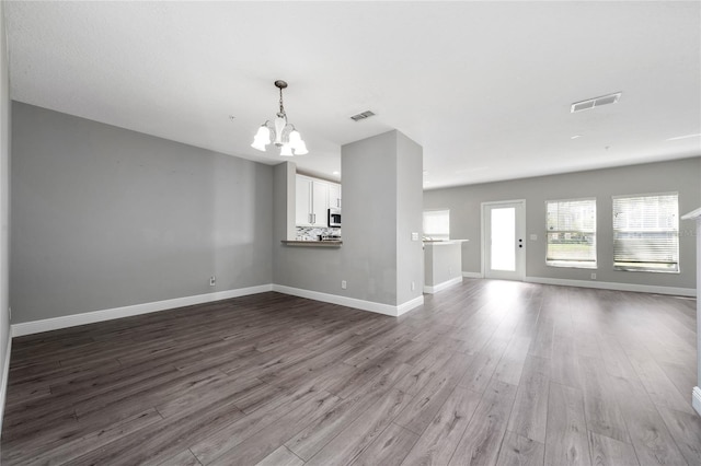 unfurnished living room with visible vents, an inviting chandelier, dark wood-type flooring, and baseboards