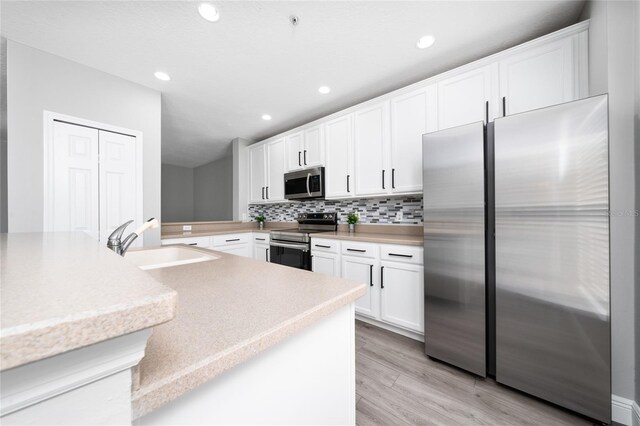 kitchen with a sink, decorative backsplash, stainless steel appliances, white cabinetry, and light wood-type flooring