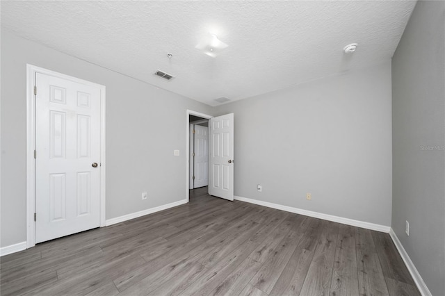unfurnished bedroom featuring visible vents, baseboards, a textured ceiling, and wood finished floors