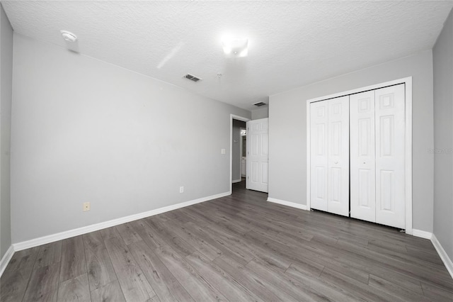 unfurnished bedroom with a closet, visible vents, baseboards, and wood finished floors
