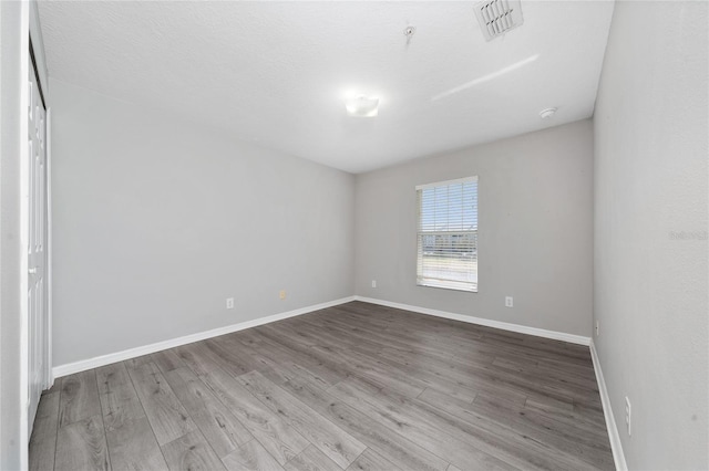 empty room featuring visible vents, wood finished floors, and baseboards