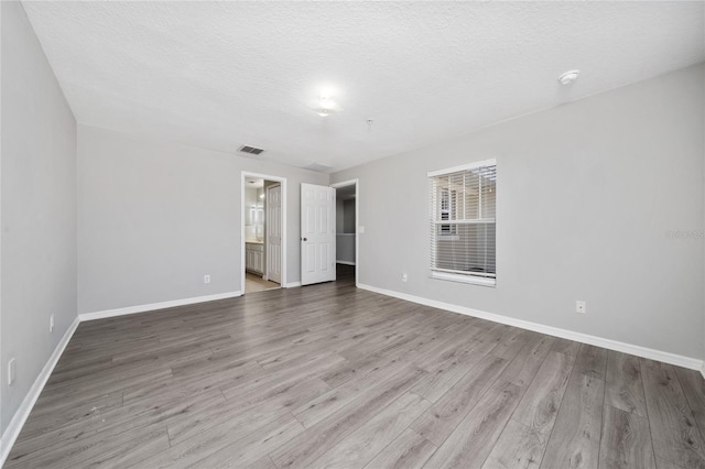empty room featuring a textured ceiling, wood finished floors, visible vents, and baseboards
