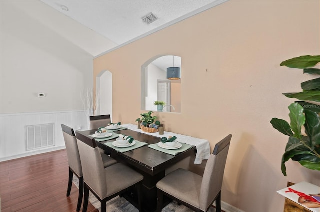 dining room with visible vents, arched walkways, dark wood finished floors, and wainscoting