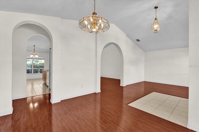 spare room featuring a notable chandelier, wood finished floors, visible vents, and arched walkways