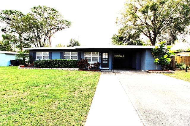 ranch-style home with an attached carport, a front lawn, fence, concrete driveway, and concrete block siding