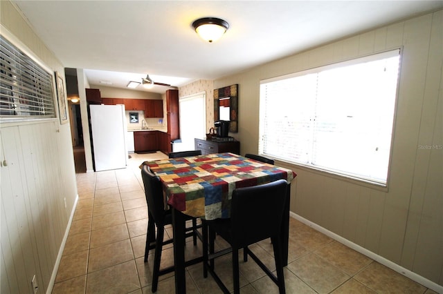 dining area with light tile patterned floors, baseboards, wooden walls, and a ceiling fan