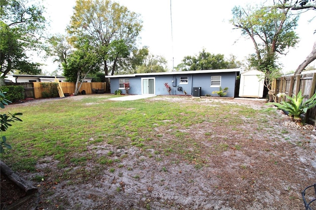 rear view of property with central air condition unit, a storage shed, a yard, an outdoor structure, and a fenced backyard